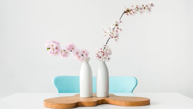 two pink petaled flowers in white vases on brown wooden surface