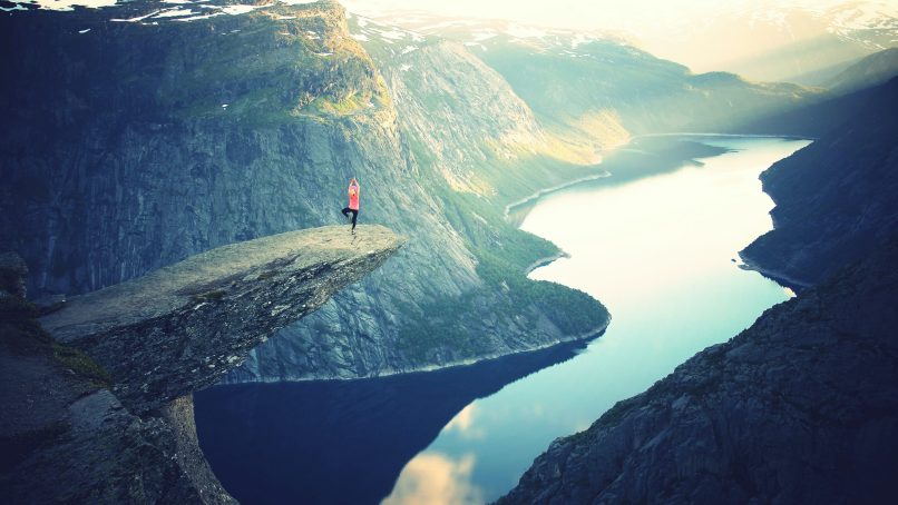 person standing on rock ledge doing yoga pose