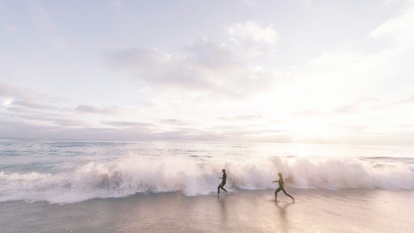 two person running on seaside beach during daytime