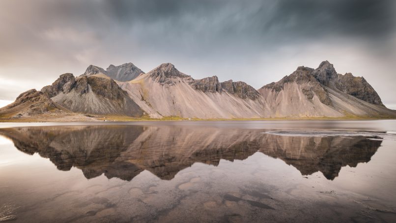 brown and white mountains near body of water under white clouds during daytime