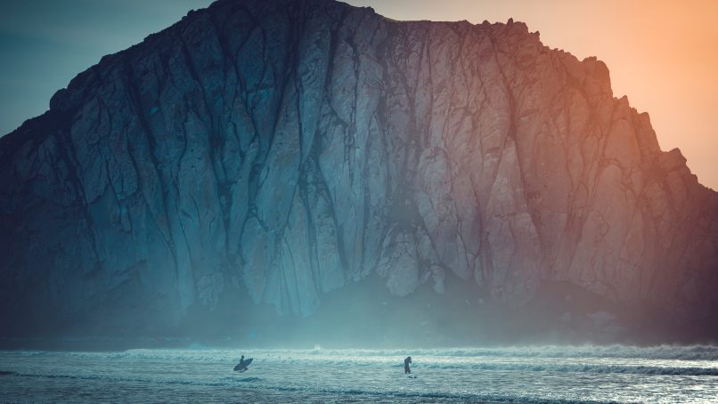 surfer on body of water near sea cliff during daytime