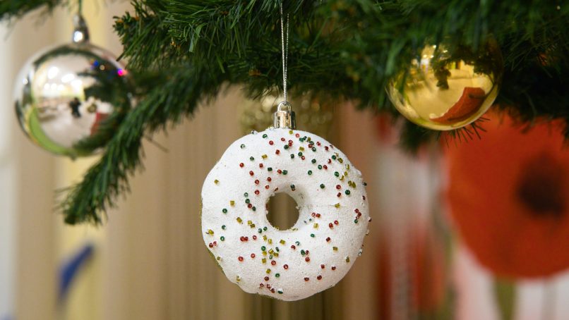 A donut ornament hangs on a christmas tree.