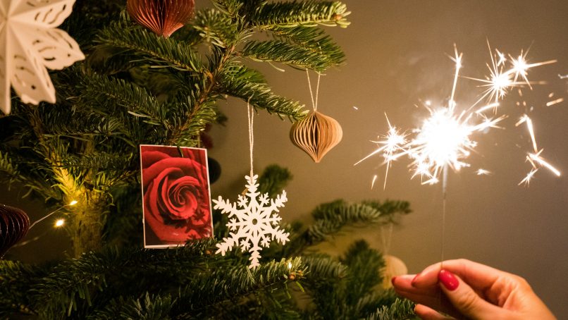 a person holding a sparkler next to a christmas tree