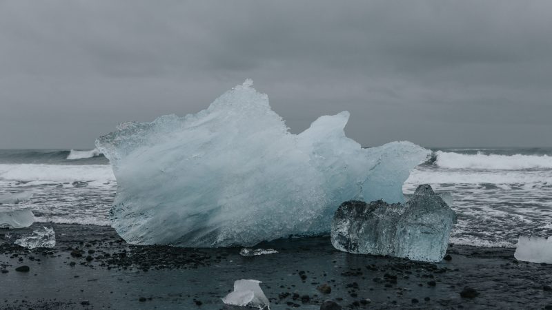 Large iceberg washed ashore on black sand beach with crashing waves. — Samsung Frame TV art