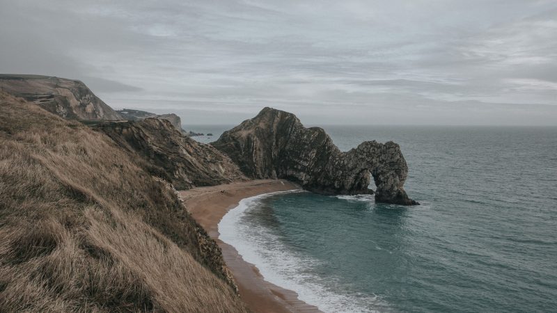Coastal view of a stone arch in the ocean with grassy cliffs — Samsung Frame TV art
